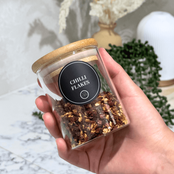 Glass jar with bamboo lid holding chili flakes, featuring round herb and spice label for pantry storage.