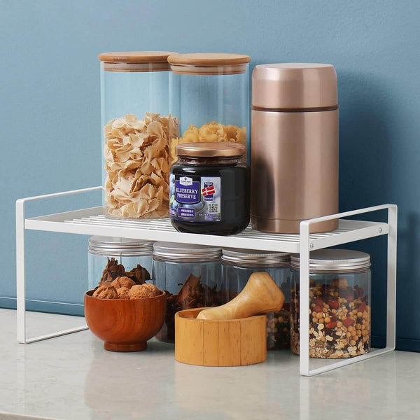 White metal under sink shelf holding pantry jars and kitchen storage containers.