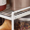 White metal under sink shelf with pantry jars and containers for kitchen storage.