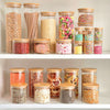 Round glass storage jars with bamboo lids on pantry shelf, ideal for kitchen organization.