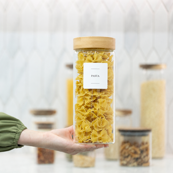 Hand holding a jar of pasta with a blurred background of other jars.