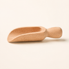 A small hand-carved wooden scoop with a smooth, rounded handle, shown on a solid light beige background.