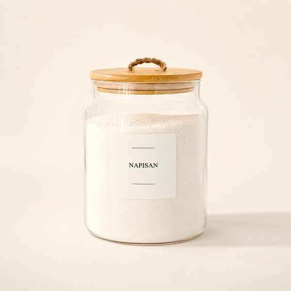 A clear glass jar filled with white napkin paper, featuring a light wood lid with a rope handle and a white label that reads 'NAPISAN'.
