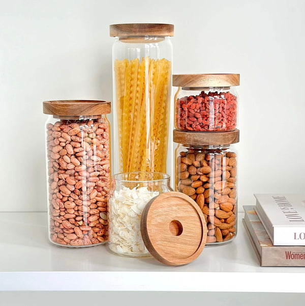 Set of five round glass acacia storage jars for pantry or kitchen organization.