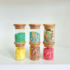 Three bamboo glass jars filled with colourful cake sprinkles, ideal for kitchen organisation and pantry use. Perfect storage organisers.