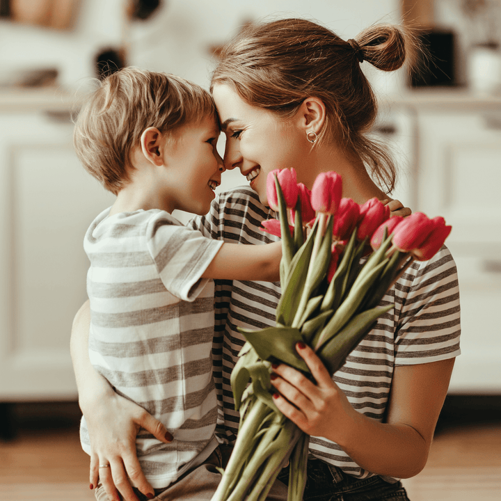 Mother and child embracing with tulips in a cozy kitchen setting.