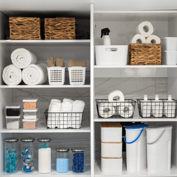Bathroom shelves with organised storage baskets, towels, jars, and cleaning supplies. Home organisation.
