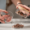 Hands using stackable round bamboo glass jars for kitchen storage with frozen fruits and nuts, offering stylish home organization solutions.
