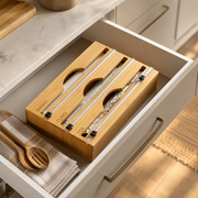 A bamboo drawer organizer set with clear plastic wrap sleeves and utensils, shown inside an open kitchen drawer.