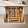A wooden drawer organizer tray holding a coordinated set of stainless steel cutlery, including knives, forks, spoons, chopsticks, and serving utensils, shown in an open kitchen drawer.