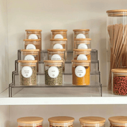 Round glass bamboo herb and spice storage jars organised on a clear tiered spice rack inside a kitchen pantry cupboard