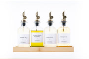 Four round glass oil dispensers with metal spouts on wood tray, ideal for kitchen storage and organisation, featuring sesame oil.