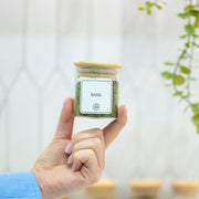 Hand holding a basil-filled Round Glass Spice Jar with Bamboo Lid – 3 Sizes for pantry organisation in a kitchen setting.