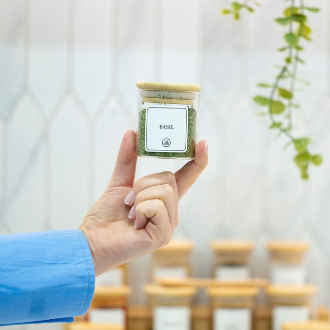 Hand holding 120ml Herb & Spice Jar with Bamboo Lid filled with basil, ideal for kitchen or pantry organisation, part of glass jar storage.