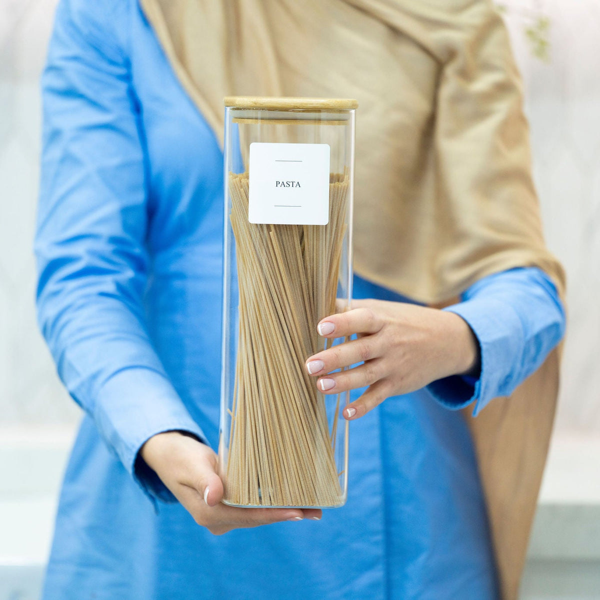 Person holding a Square Glass Jar with Bamboo Lid – 2300ml Pantry Storage filled with pasta for kitchen organisation.