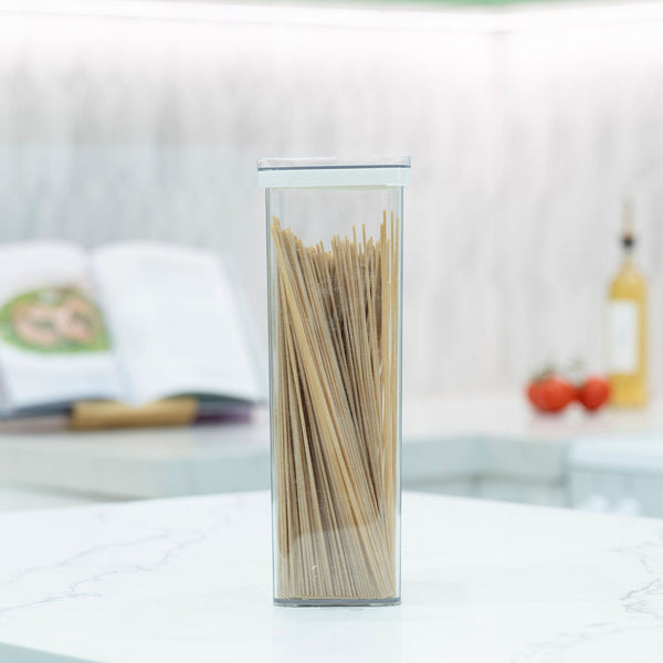 Tall clear airtight pantry container filled with spaghetti on a white marble kitchen bench