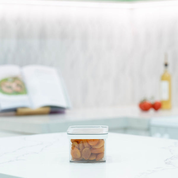 Small clear airtight pantry container filled with dried apricots on a white marble benchtop
