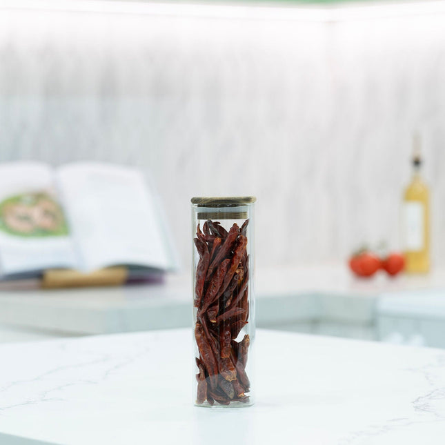 Tall glass jar from the Acacia Square Pantry Collection filled with dried chillies on a kitchen countertop.