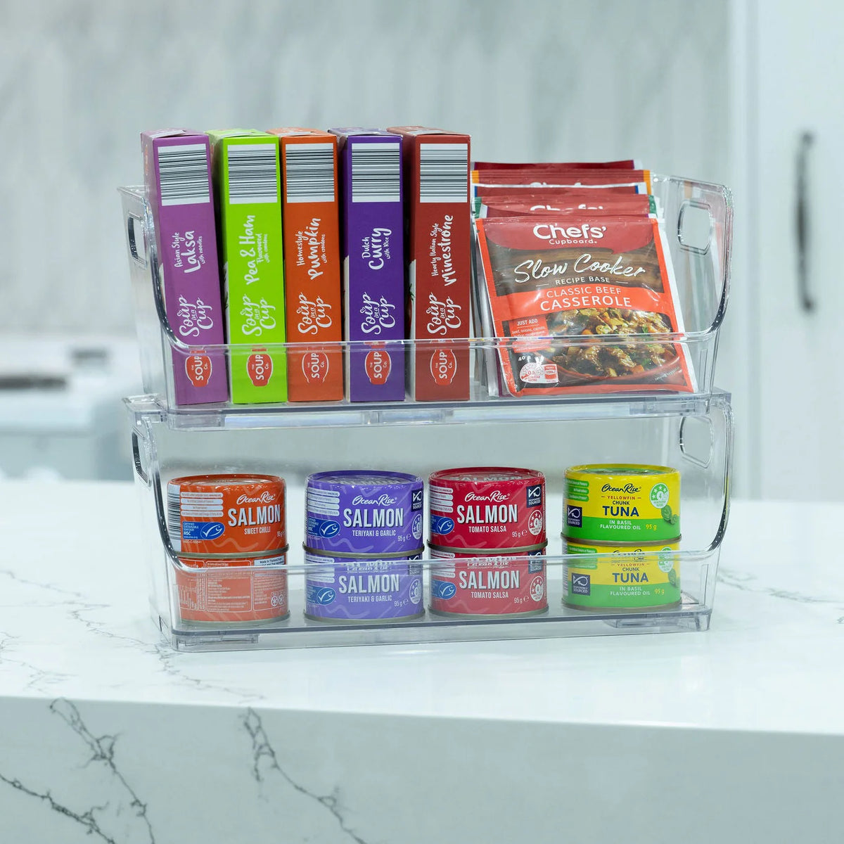 Stacked acrylic pantry organisers holding various food items in a kitchen setting, part of the Family Pantry System Pack for efficient storage.