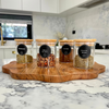 Four clear glass spice jars with bamboo lids on a wooden tray, featuring spice labels, ideal for stylish kitchen organisation.
