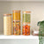 Round glass bamboo storage jars set with assorted pantry items on a shelf.