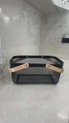 Black metal kitchen basket with wooden handles, ideal for pantry or under sink storage.
